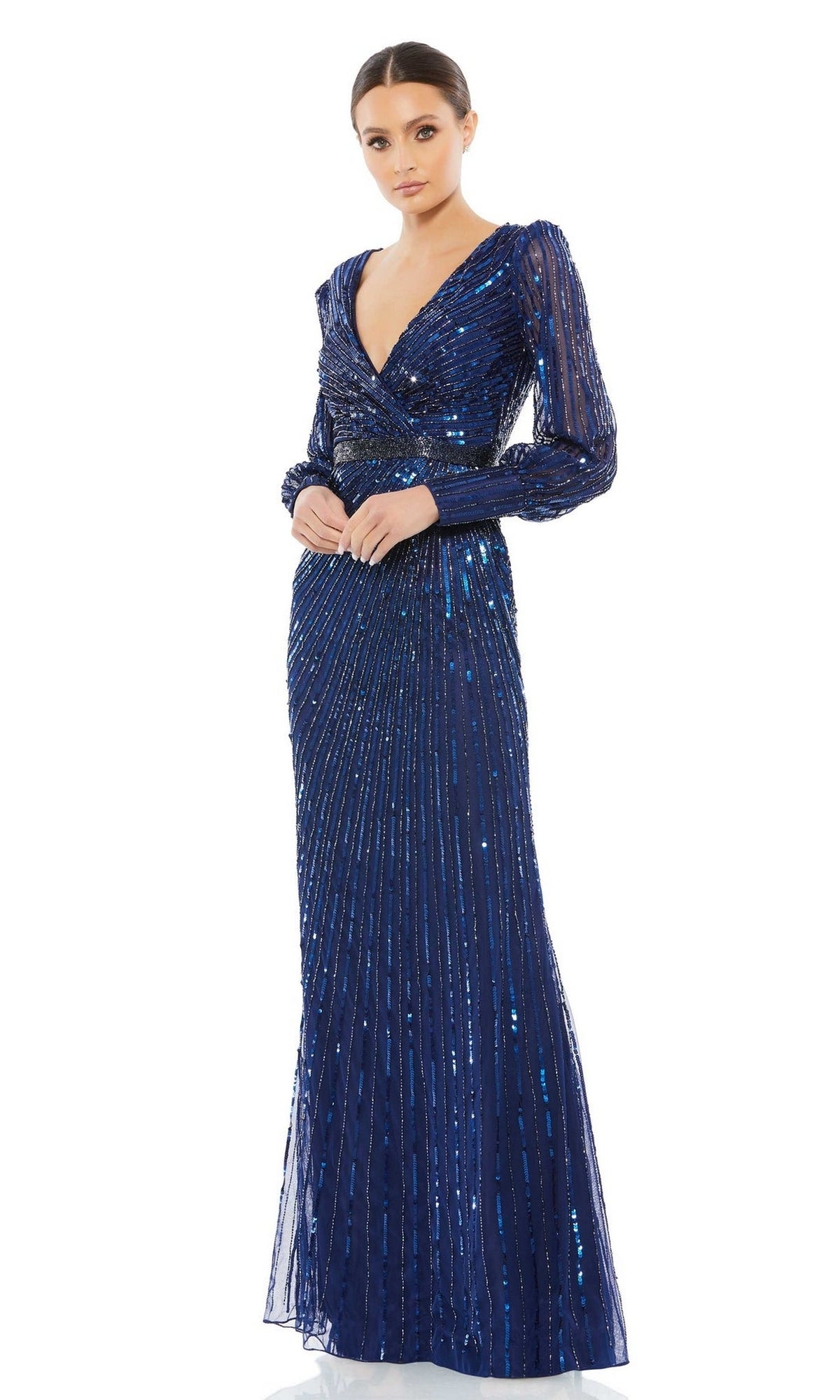 A woman in the Mac Duggal 5501 long sleeve sequin formal dress, featuring a deep blue hue and V-neckline, stands against a white background—an elegant gown ideal for any mother of the bride.